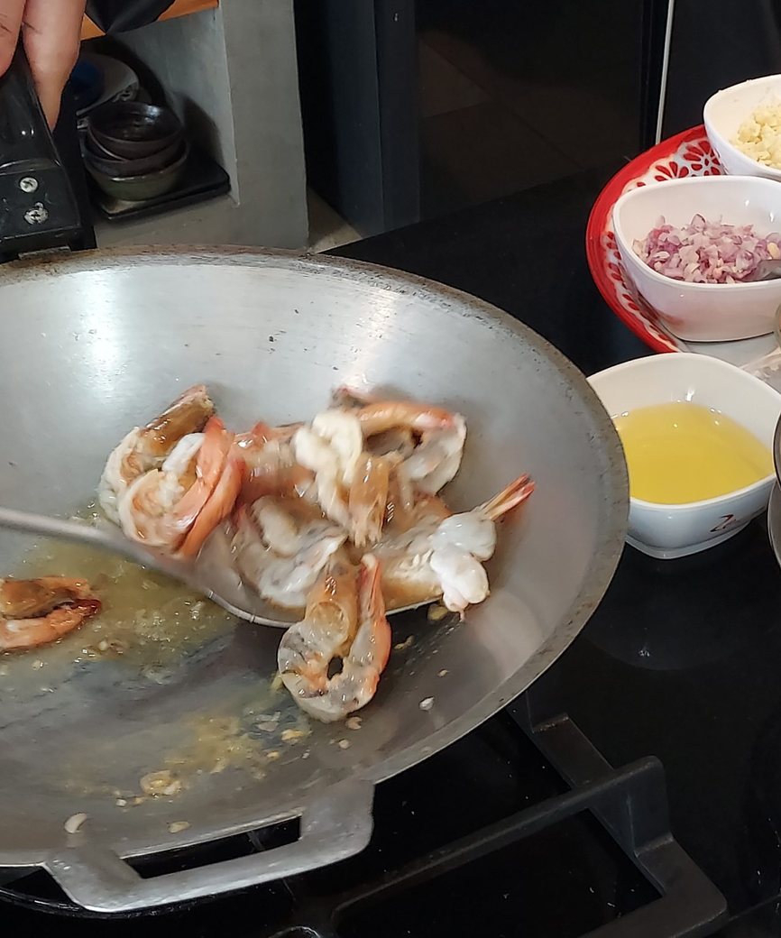 Shrimp being stir-fried in a wok on a stovetop, with prepared ingredients nearby